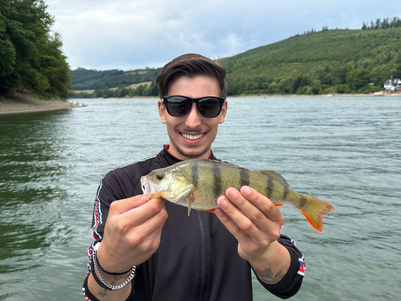 Angler mit Barsch und Sonnenbrille an der Talsperre